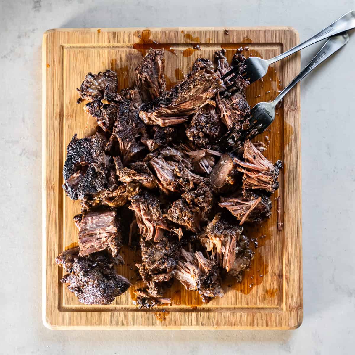 Forks resting next to a roughly shredded beef chuck roast on a cutting board.