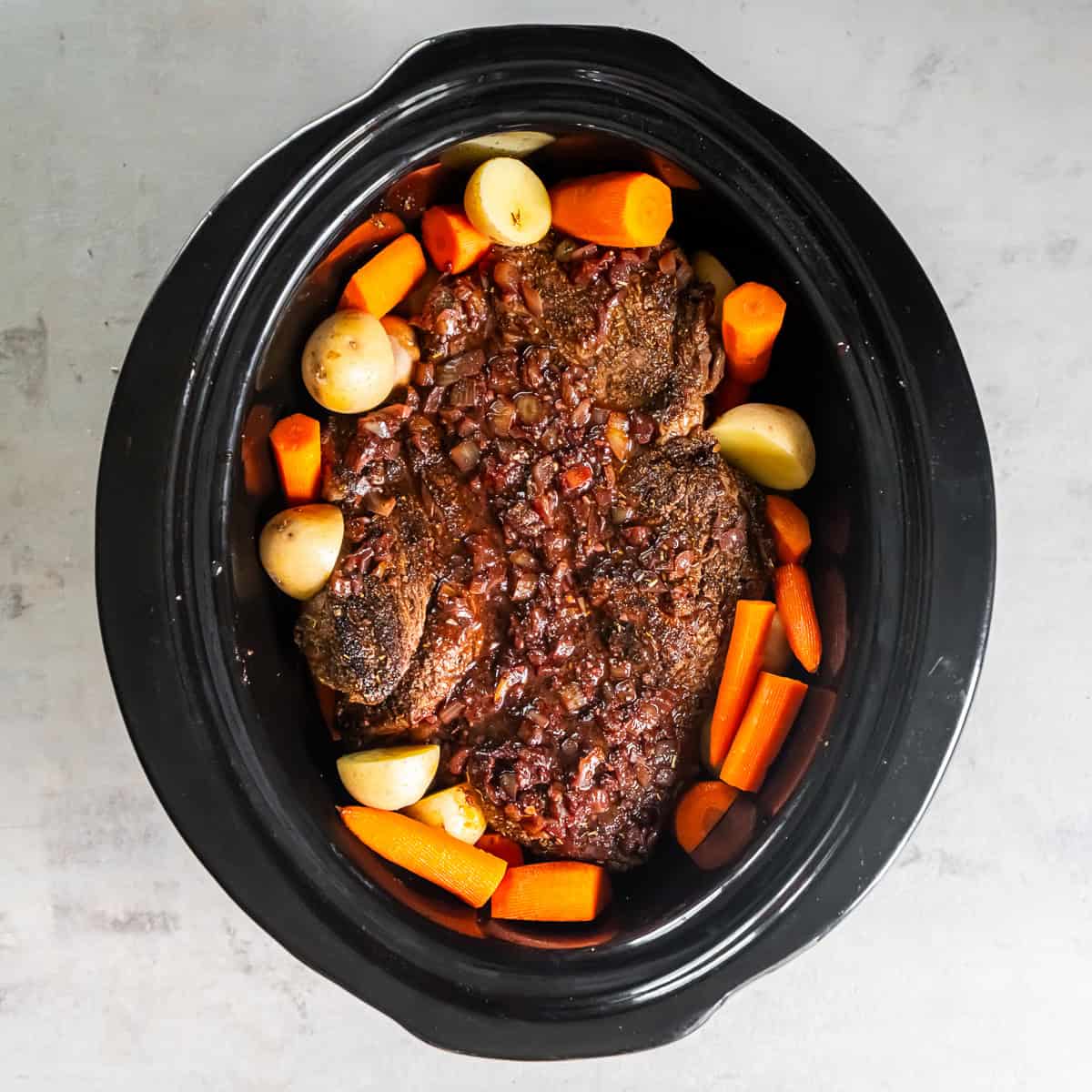 Chuck roast in a slow cooker with potatoes and carrots.