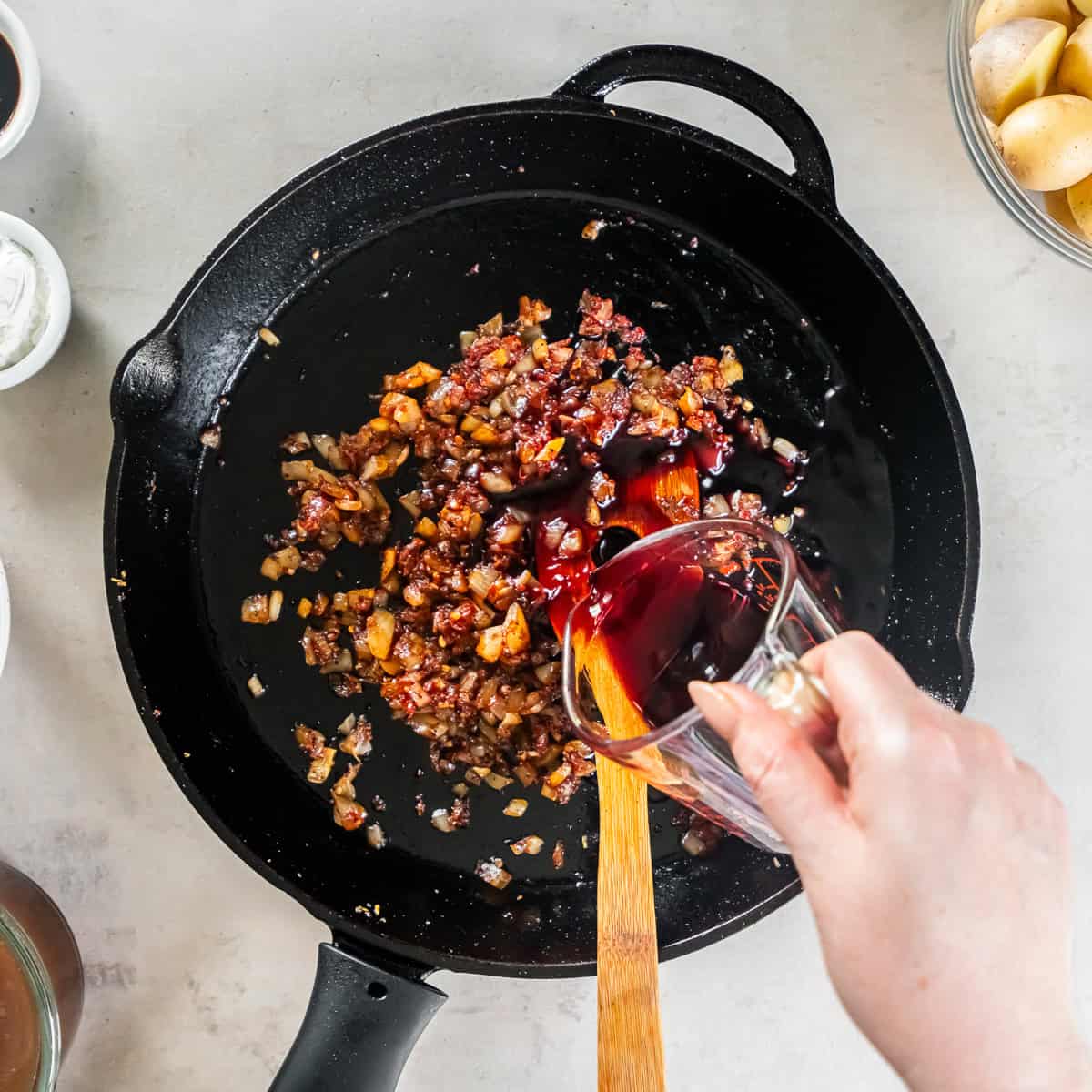 Red wine pouring into an onion mixture in a cast iron skillet.