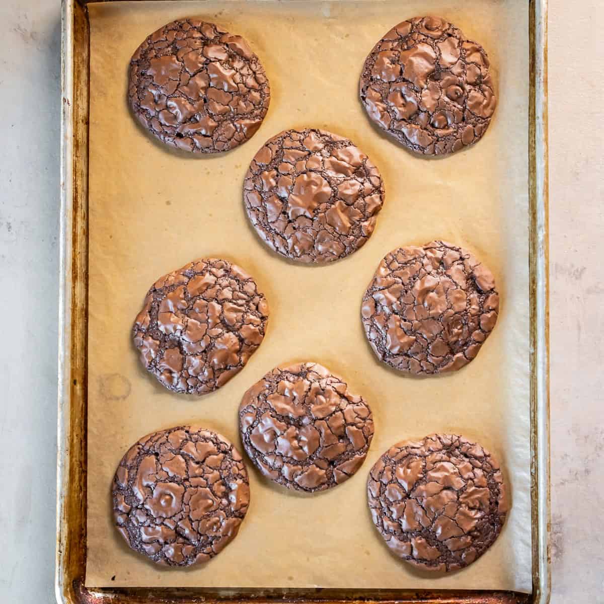 Eight freshly baked brownie mix cookies with shiny, crackly chocolate tops on a parchment-lined baking sheet.