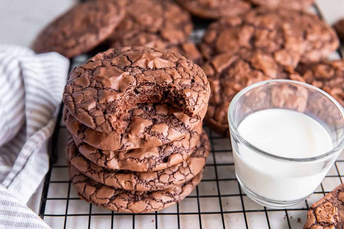 Stack of brownie mix cookies with shiny, crackly tops and a bite taken out of the top cookie, next to a glass of milk.