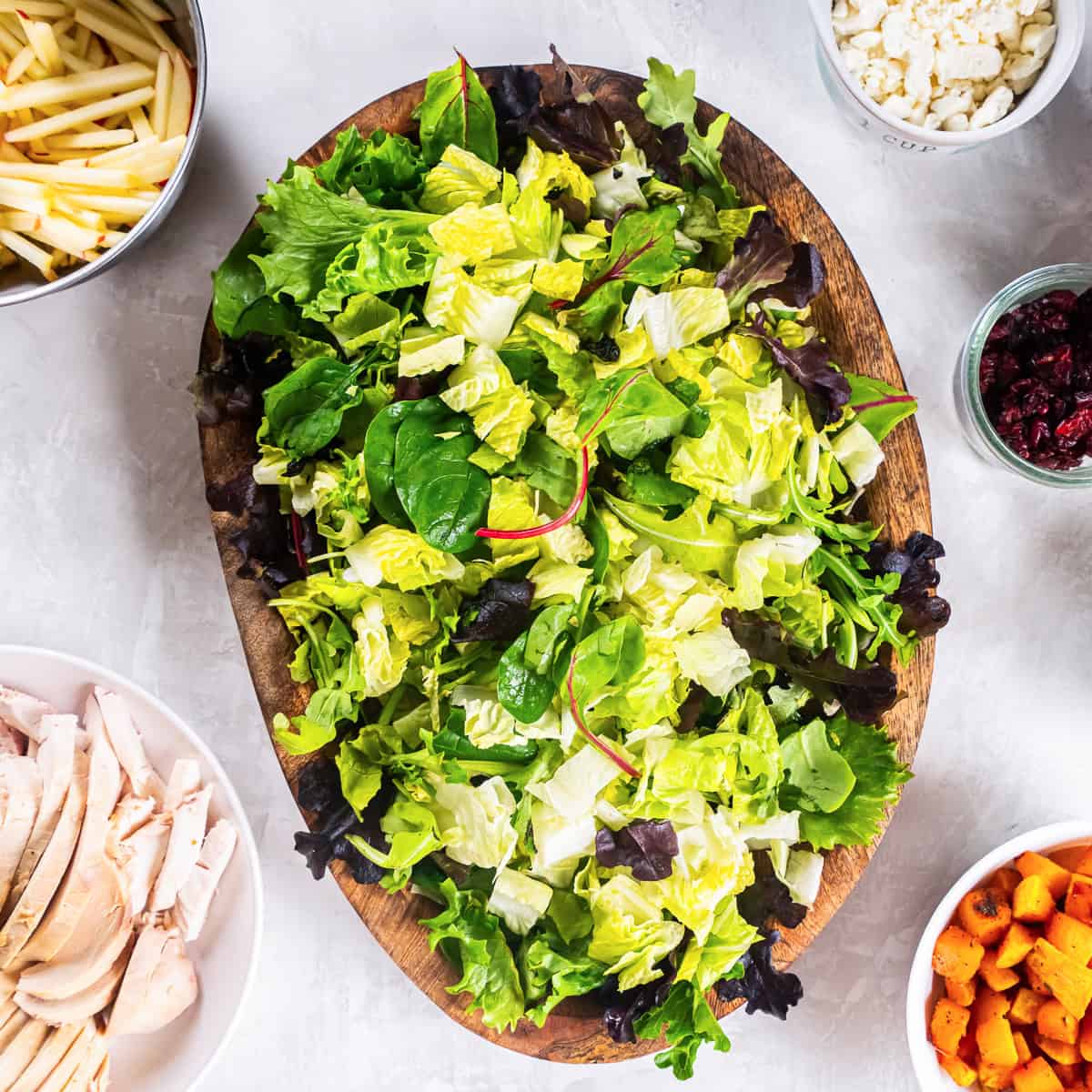 A mixture of fresh baby greens and chopped romaine arranged on a large wooden serving platter.