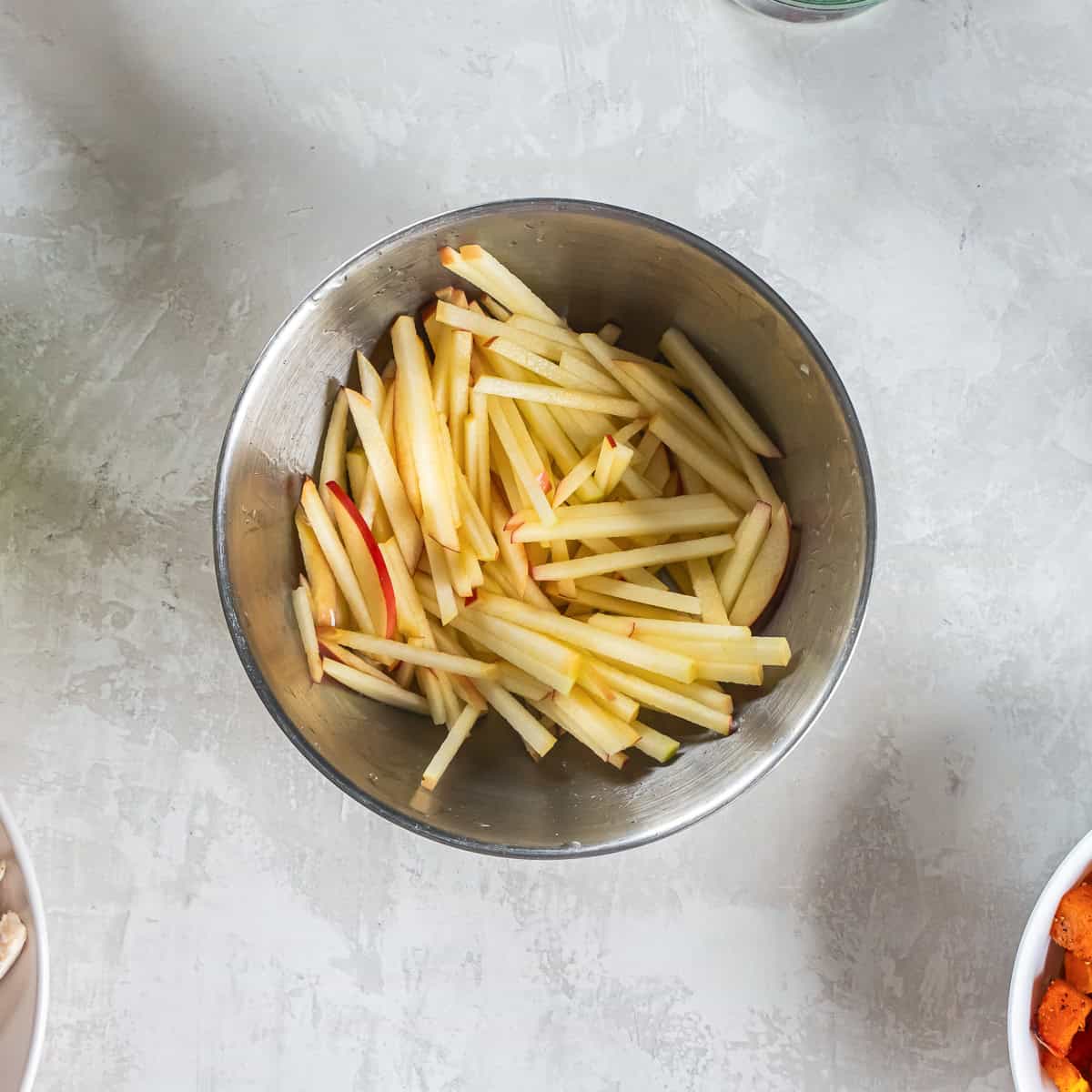 Thin apple matchsticks with the peel left on in a metal bowl.
