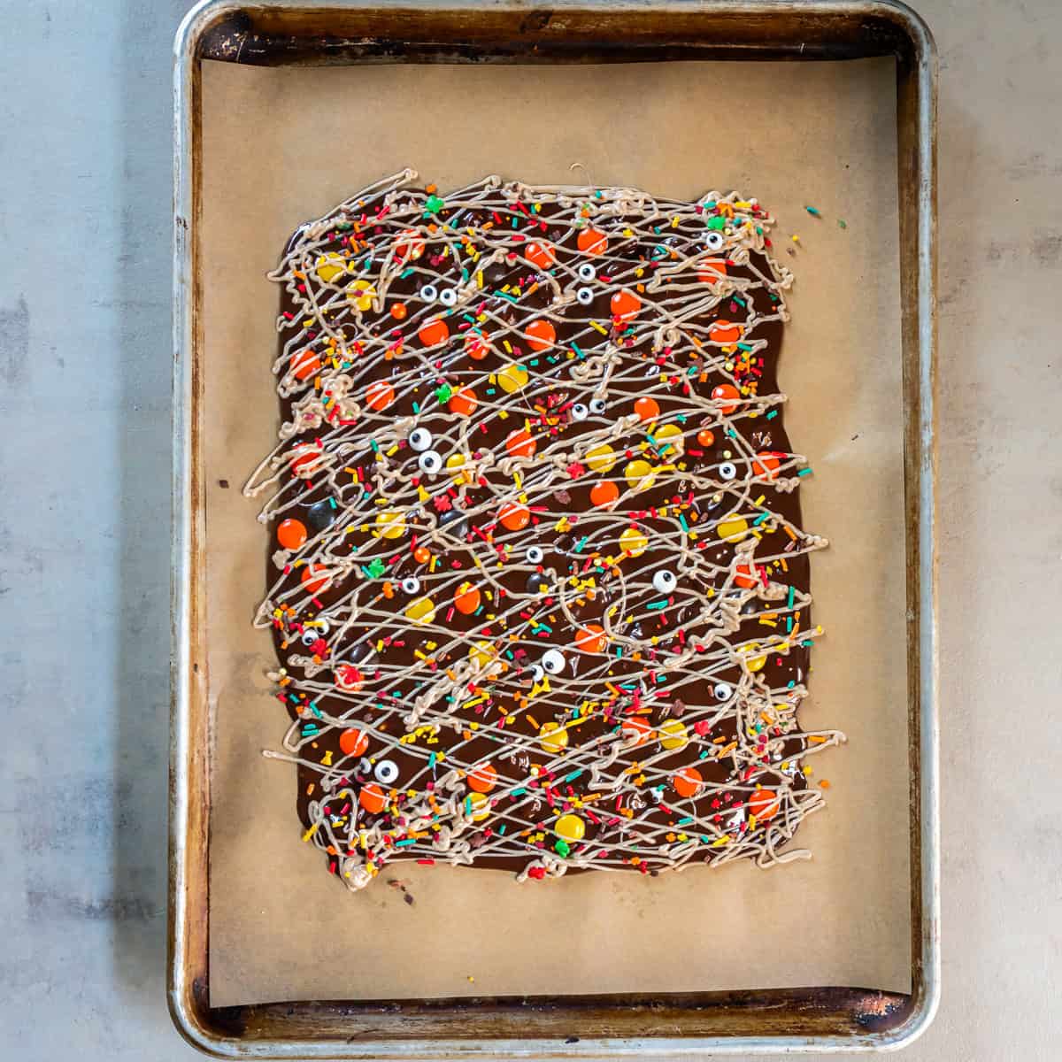 Halloween Bark topped with white chocolate drizzle, Reese’s Pieces, colorful sprinkles, and candy eyeballs, ready to chill.