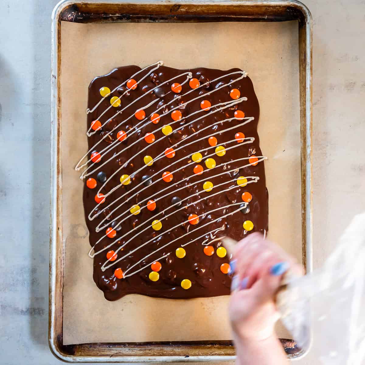 Drizzling pumpkin spice white chocolate over chocolate bark topped with Reese’s Pieces.