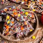Halloween chocolate bark piled on a rustic plate, topped with white chocolate drizzle, Reese’s Pieces, colorful sprinkles, and candy eyeballs.