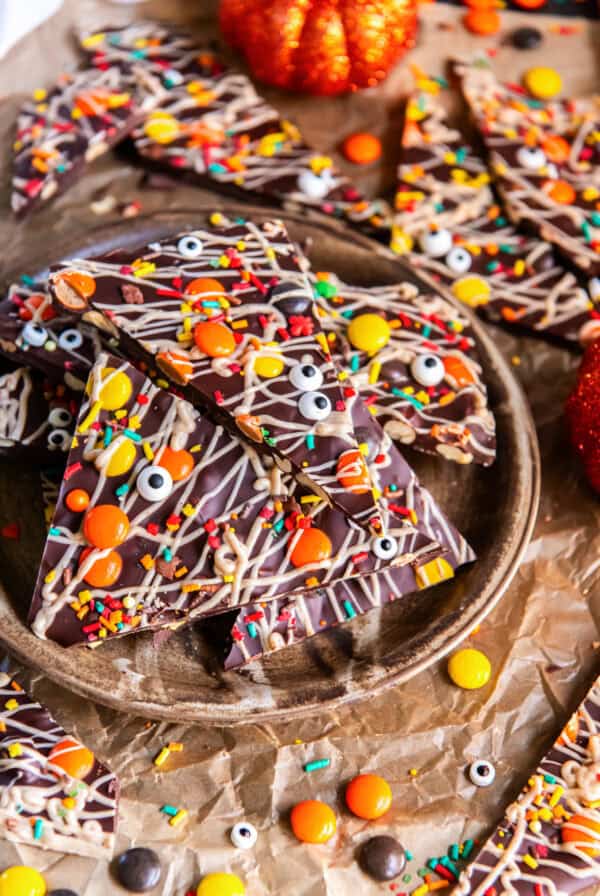 Halloween chocolate bark piled on a rustic plate, topped with white chocolate drizzle, Reese’s Pieces, colorful sprinkles, and candy eyeballs.