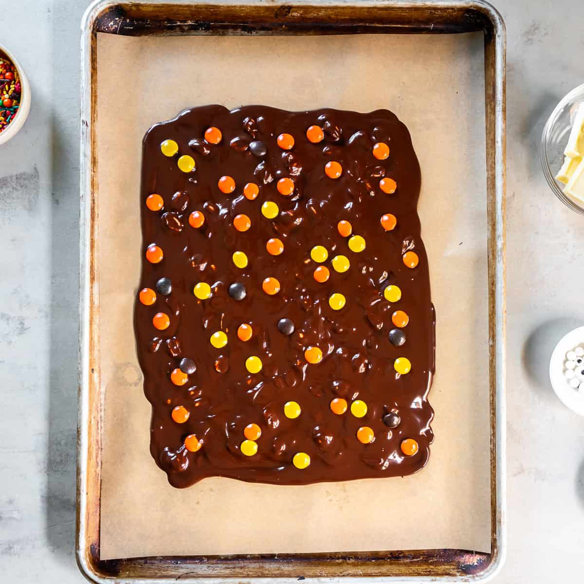 Reese’s Pieces scattered over the chocolate bark base on a parchment-lined baking sheet.