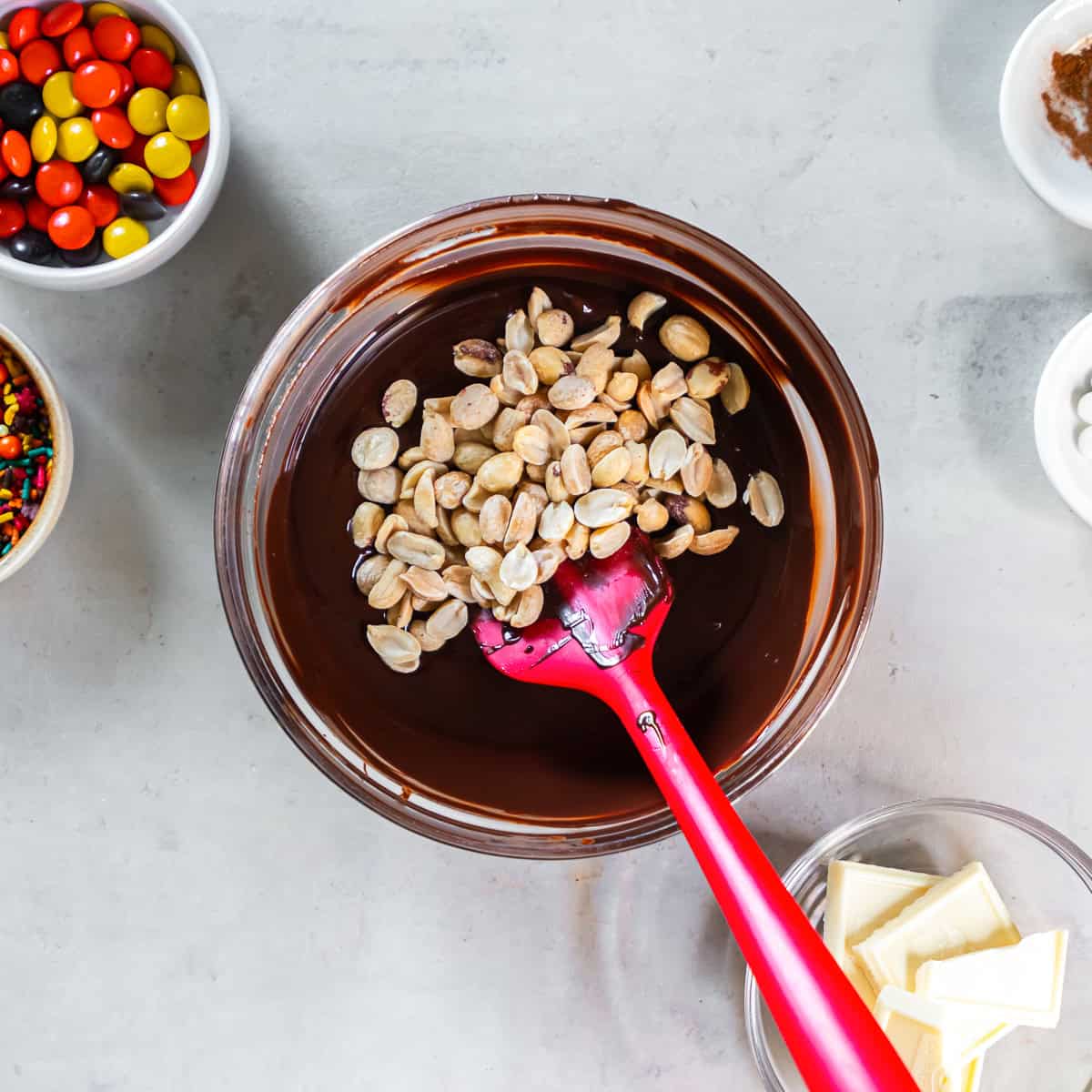 Roasted salted peanuts added to melted semisweet chocolate in a glass bowl.