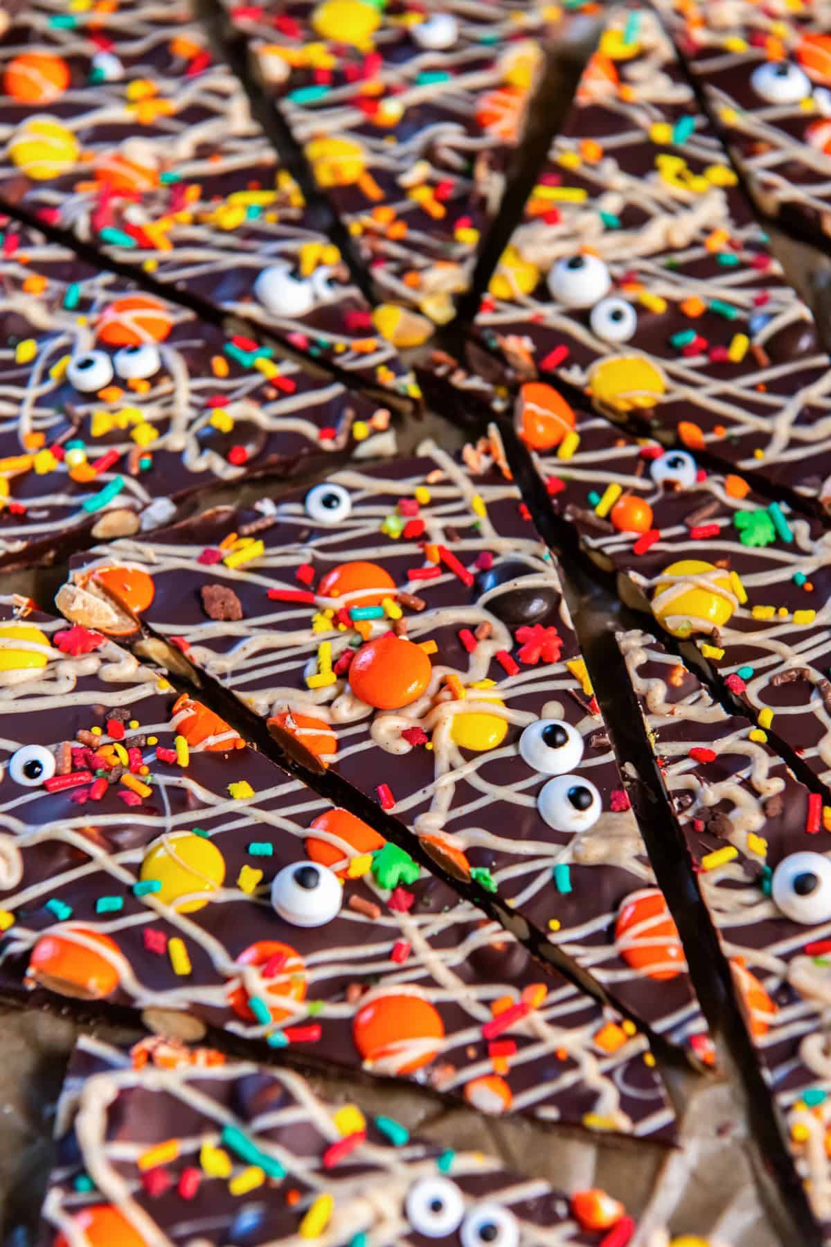 Close-up of Halloween chocolate bark pieces topped with pumpkin spice white chocolate drizzle, Reese’s Pieces, colorful sprinkles, and candy eyeballs.