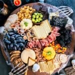 Halloween charcuterie board filled with pumpkin-shaped cheese balls, sliced cheeses, cured meats, grapes, figs, blackberries, olives, crackers, almonds, popcorn, chocolate, and candy, surrounded by cobwebs, spiders, skulls, candles, and skeleton hands.