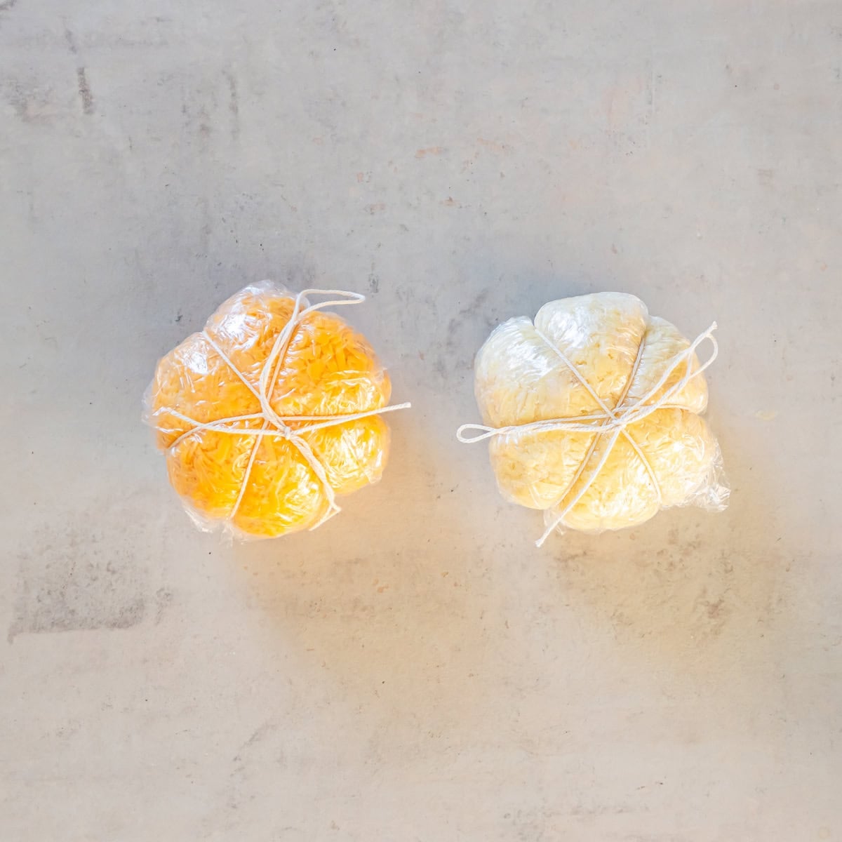 Two plastic-wrapped Boursin cheese pumpkins, one white and one orange, tied with kitchen twine to create pumpkin-shaped ridges on a white plate.