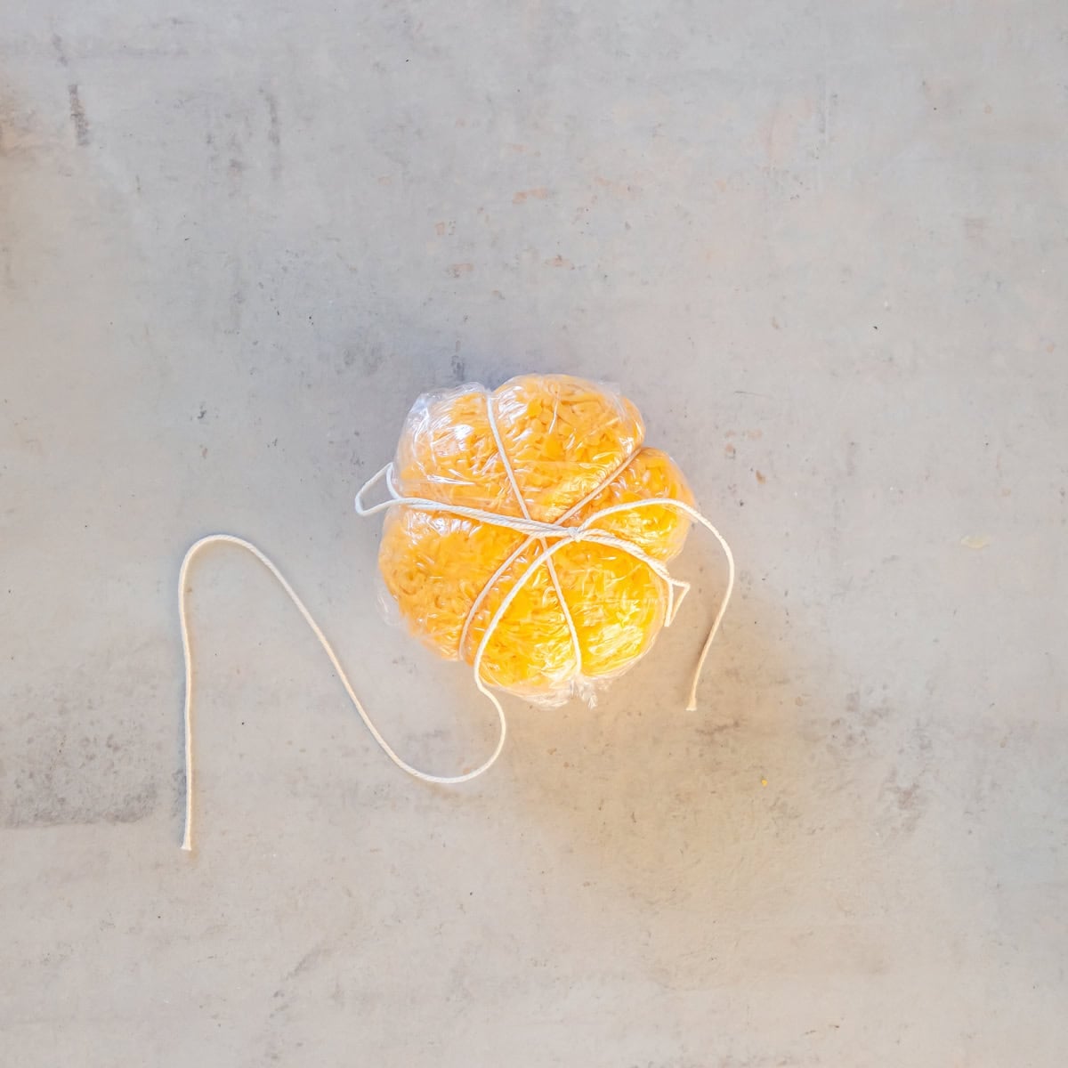 Orange cheddar-coated Boursin cheese ball wrapped in plastic and secured with kitchen twine to create six pumpkin-shaped sections.