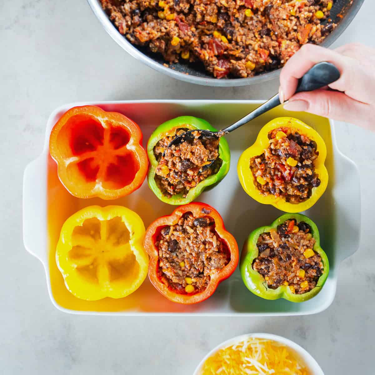 Spooning Mexican ground beef and rice filling into hollowed out bell peppers.