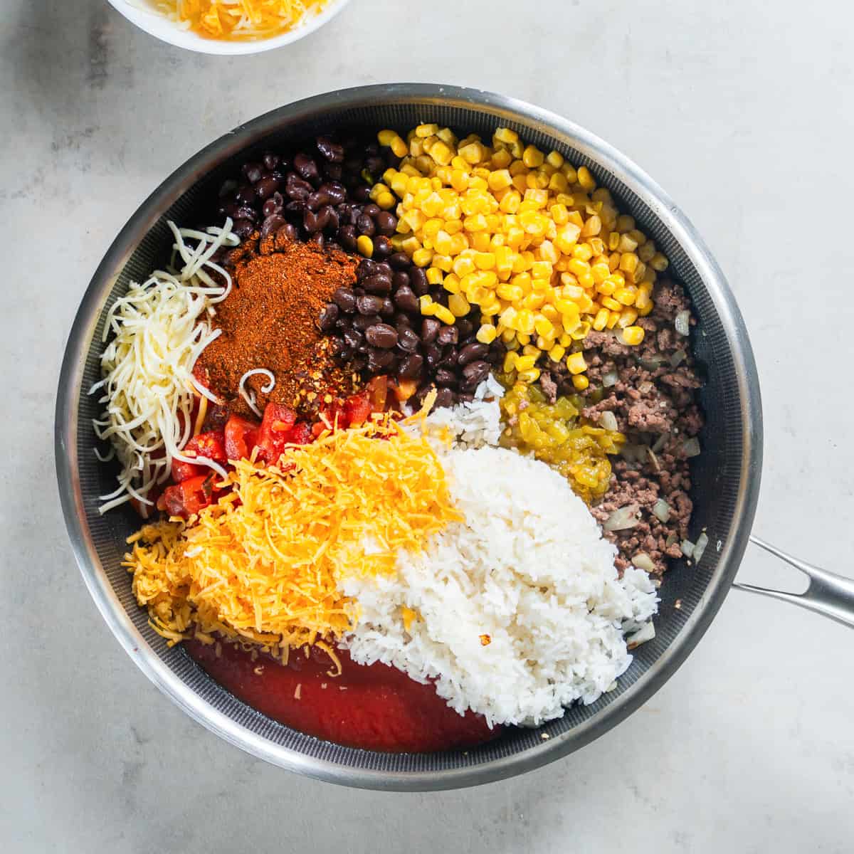 Ground beef, rice, black beans, corn, tomatoes, green chiles, taco seasoning, and cheese in a skillet.