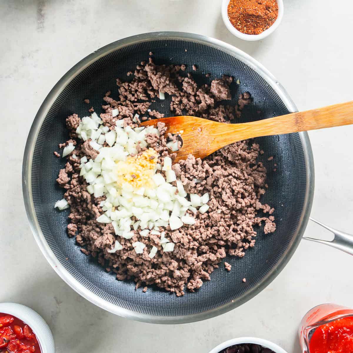 Cooked ground beef with diced onion and minced garlic in a skillet.