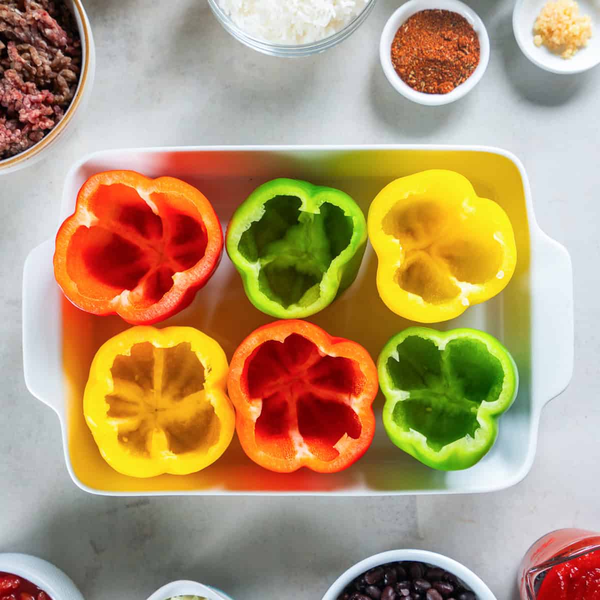Hollowed out red, yellow, and green bell peppers arranged in a baking dish.