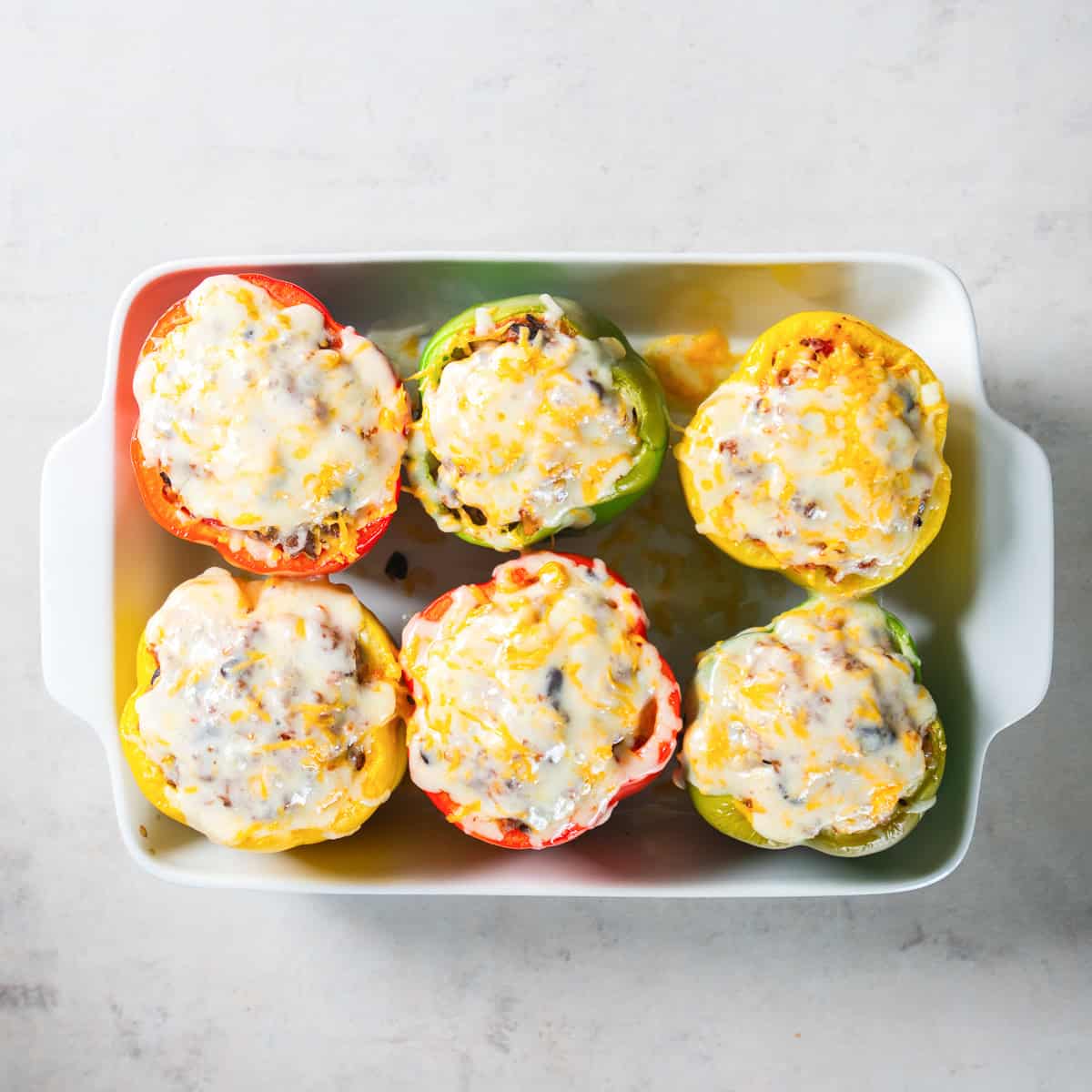 Baked Mexican stuffed peppers topped with melted cheese in a white baking dish.
