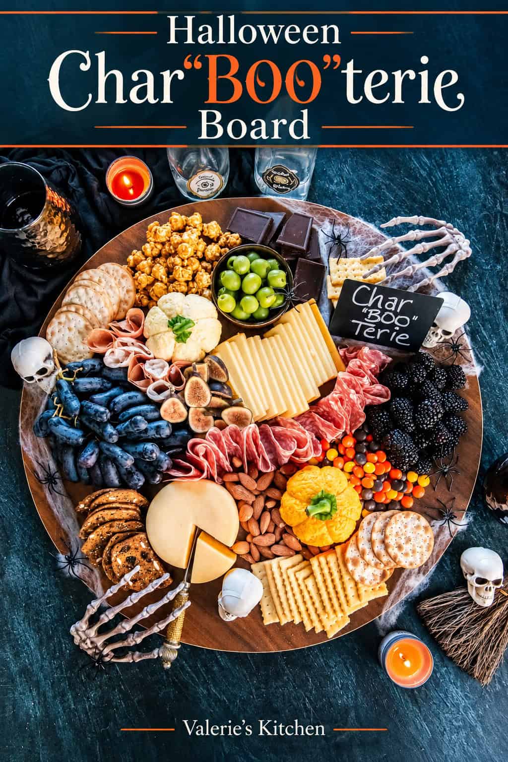 Pinterest graphic with “Halloween CharBOOterie Board” text above a festive charcuterie spread with pumpkin-shaped cheese balls, cured meats, cheeses, fruit, crackers, candy, and spooky skeleton and spider decorations.