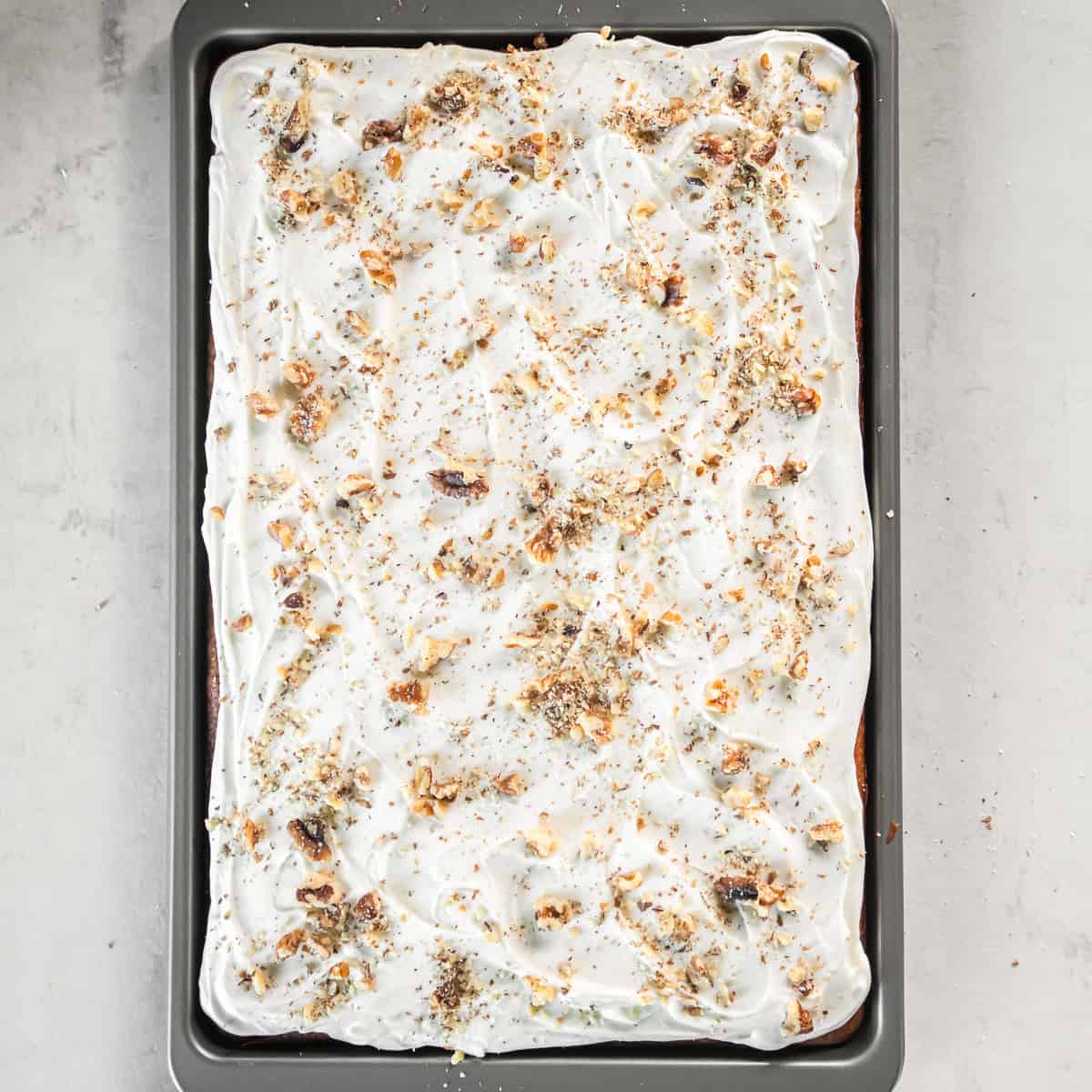 Cream cheese frosting with walnuts and cinnamon on pumpkin bars in a baking sheet.