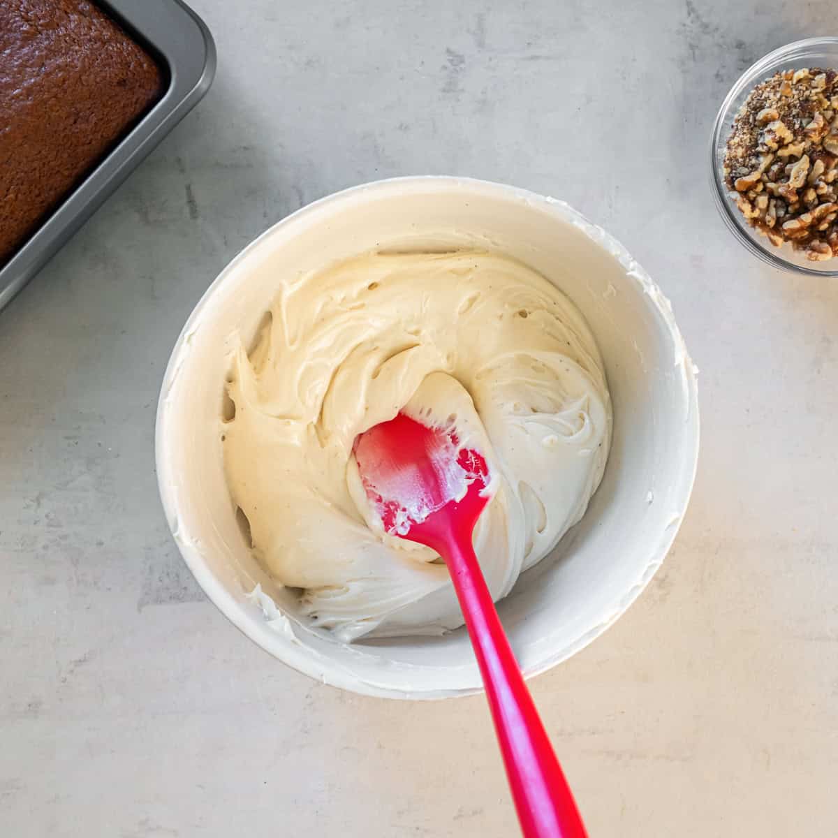 Smooth cream cheese frosting in a mixing bowl with a red spatula.