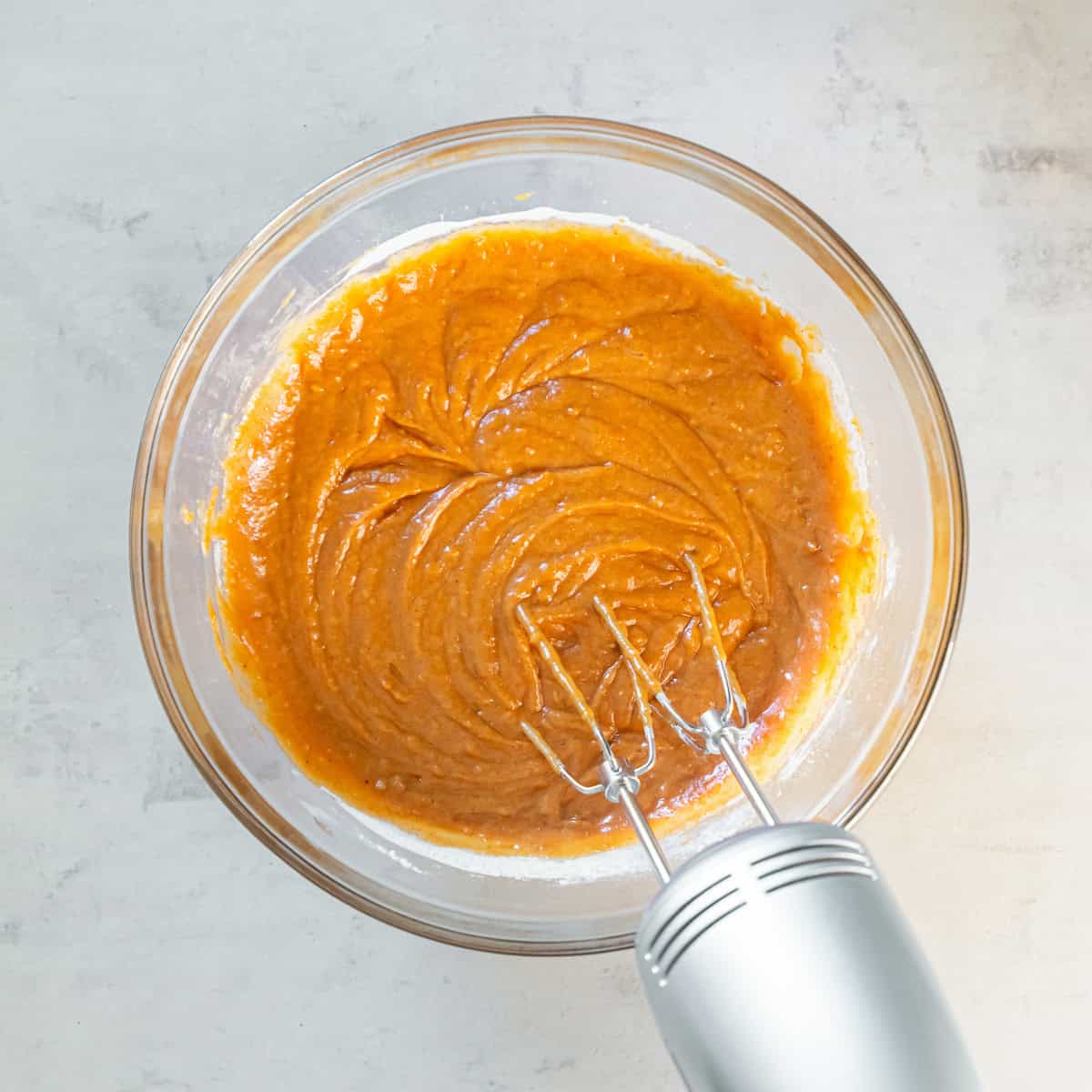 Pumpkin bar batter being mixed with an electric hand mixer in a glass bowl.