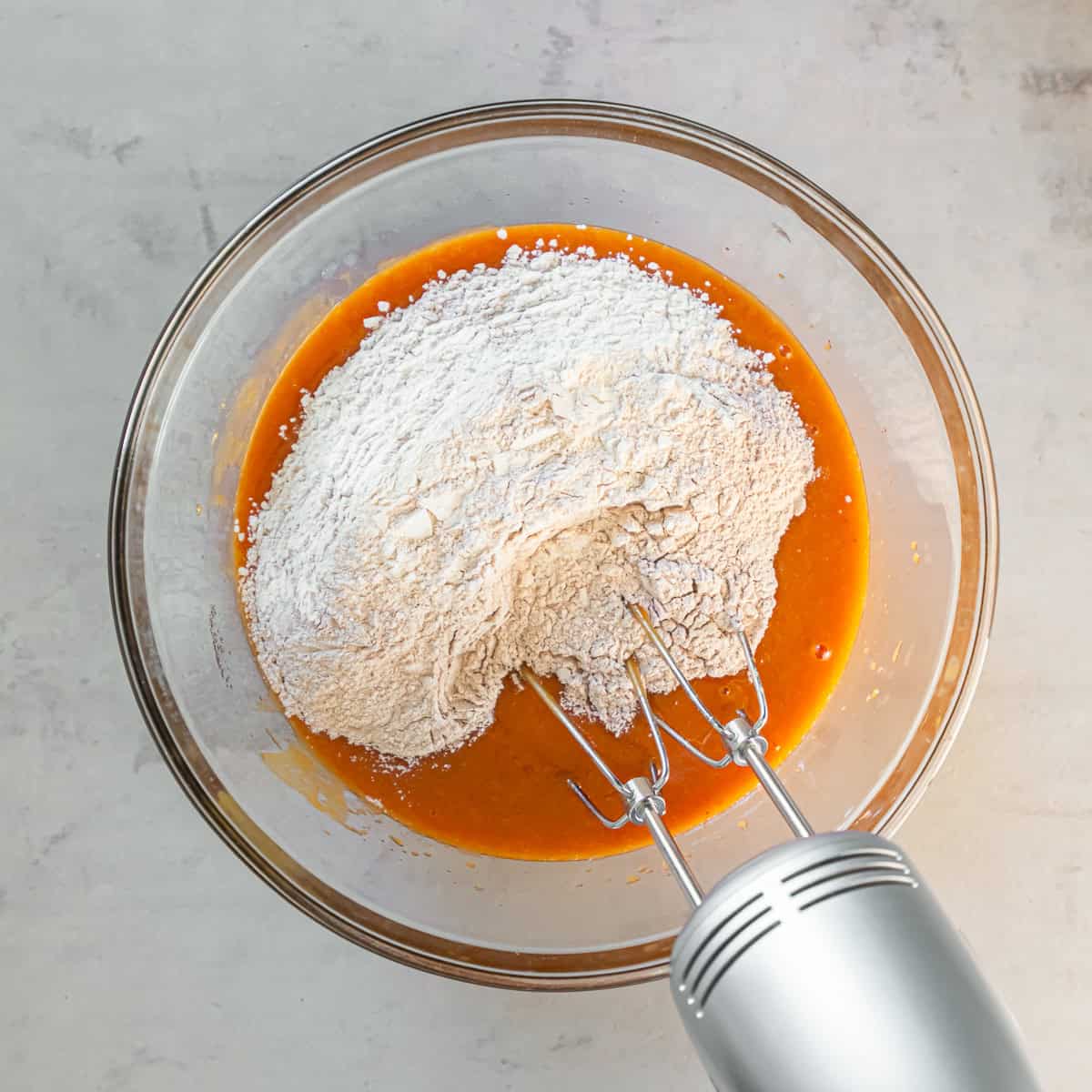 Dry ingredients added to the pumpkin mixture with the electric mixer ready to combine the batter.