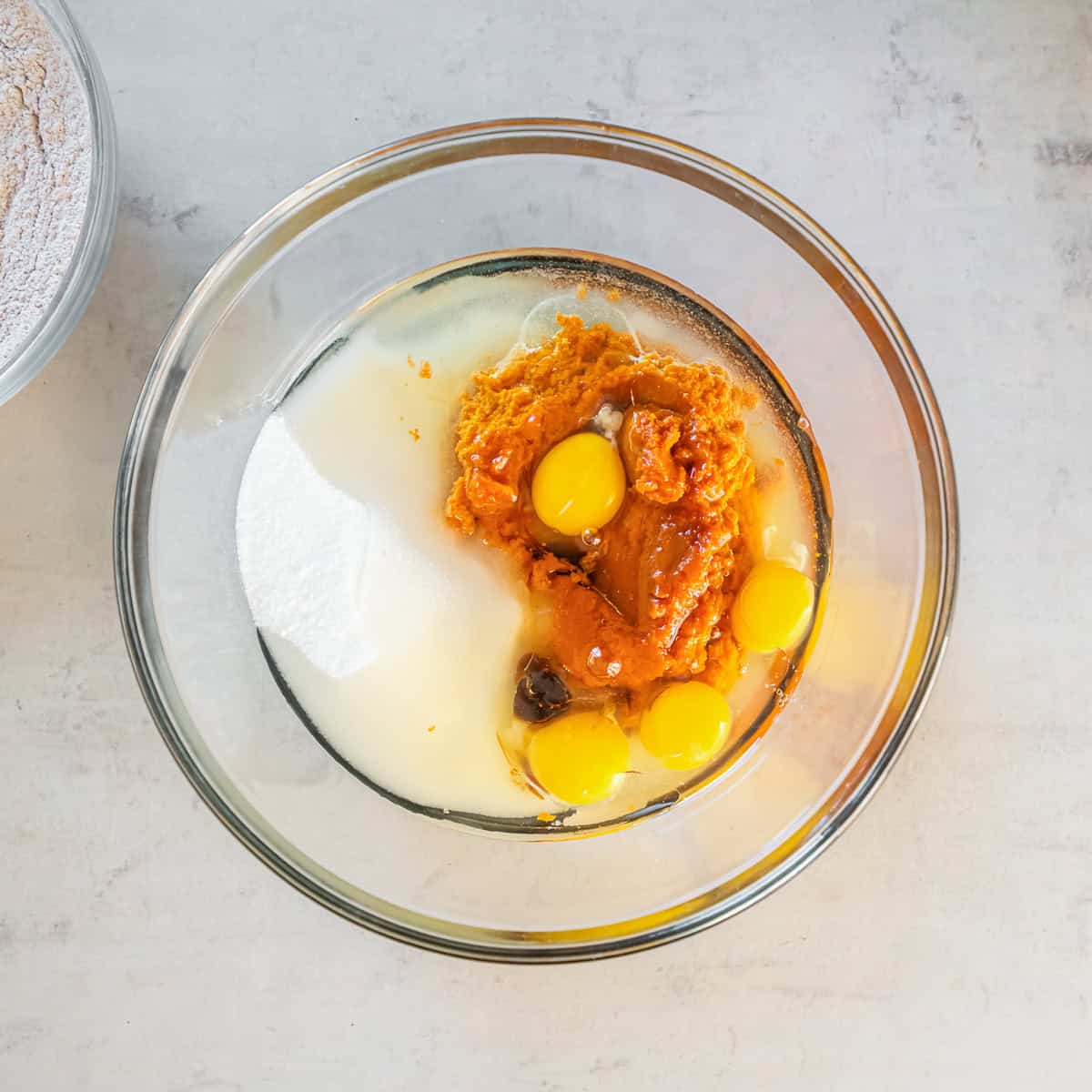 Pumpkin puree, sugar, eggs, oil, and vanilla combined in a large glass mixing bowl.