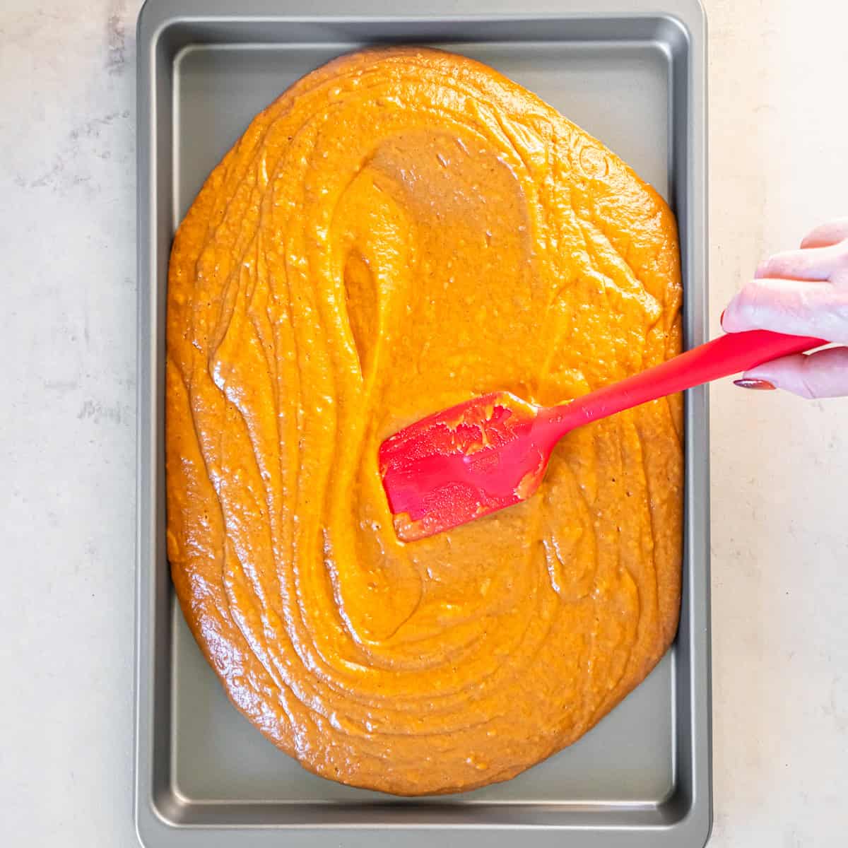 Pumpkin batter being spread evenly in a 15- by 10-inch baking pan with a spatula.