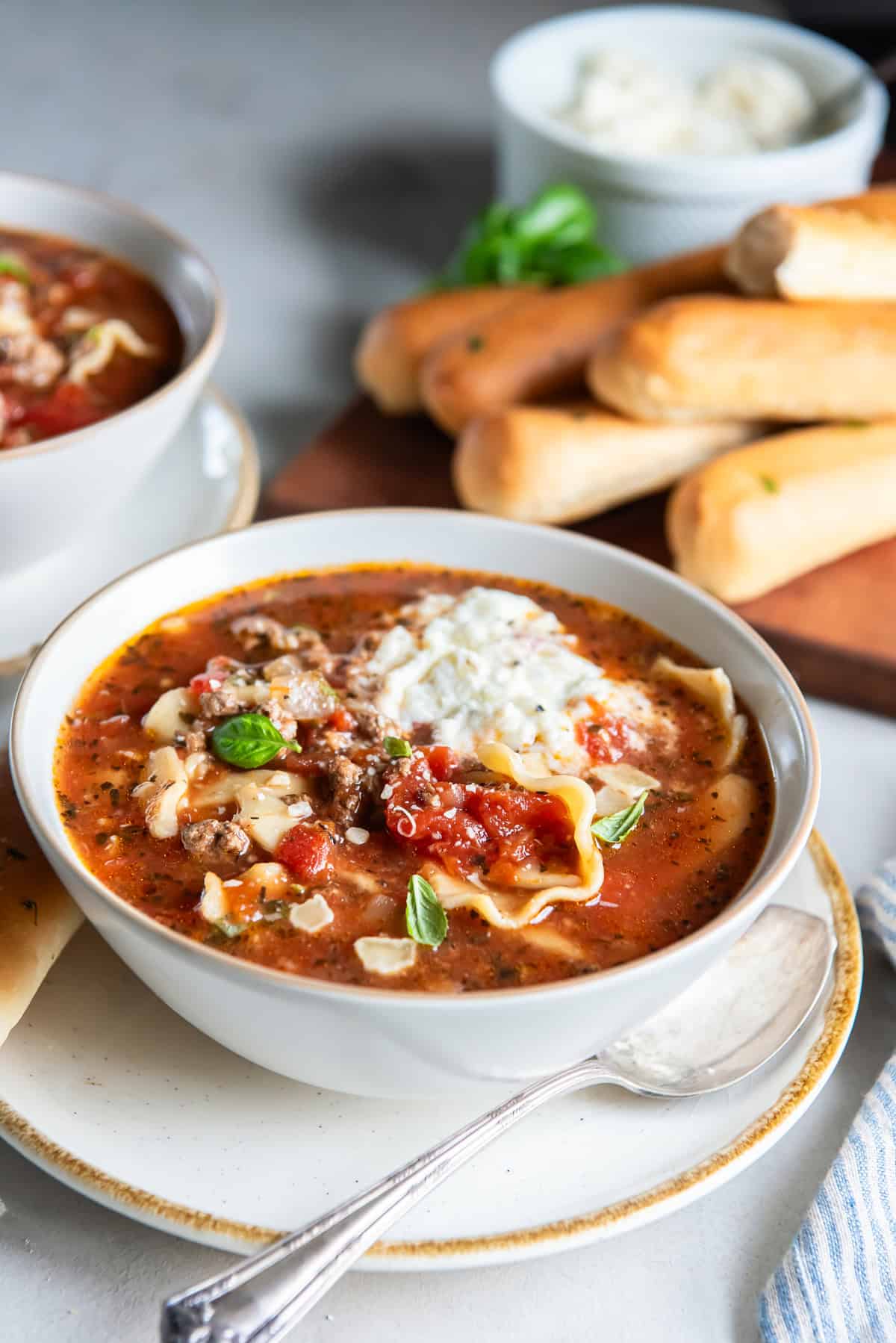 A bowl of slow cooker lasagna soup with a pile of soft breadsticks behind it.
